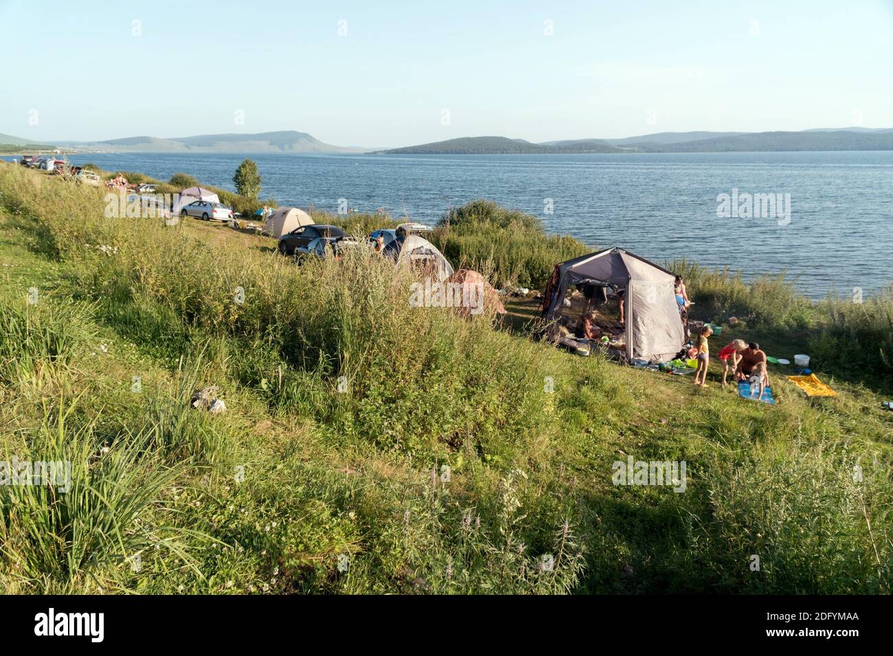 Tents with people resting on the shores of the Big Lake during their vacation on a sunny summer day. Stock Photo