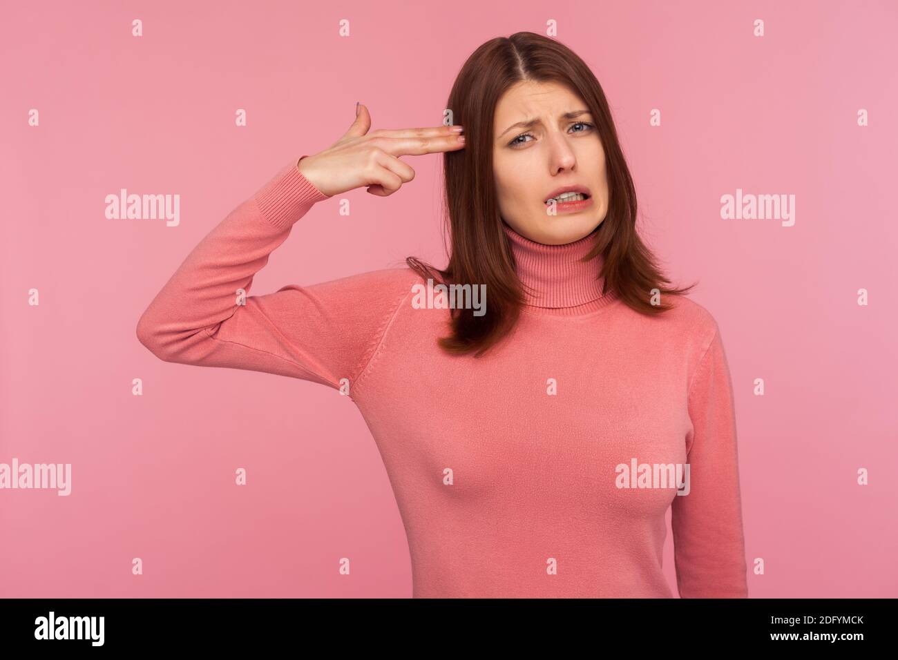 Sad frustrated brunette woman holding fingers near head imitating gun, looking at camera with panic stressed expression. Indoor studio shot isolated o Stock Photo