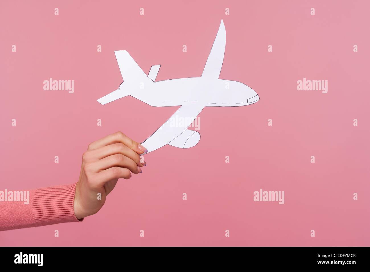 Closeup female hand holding paper plane, plane arrival and departure, travelling abroad, airline service. Indoor studio shot isolated on pink backgrou Stock Photo