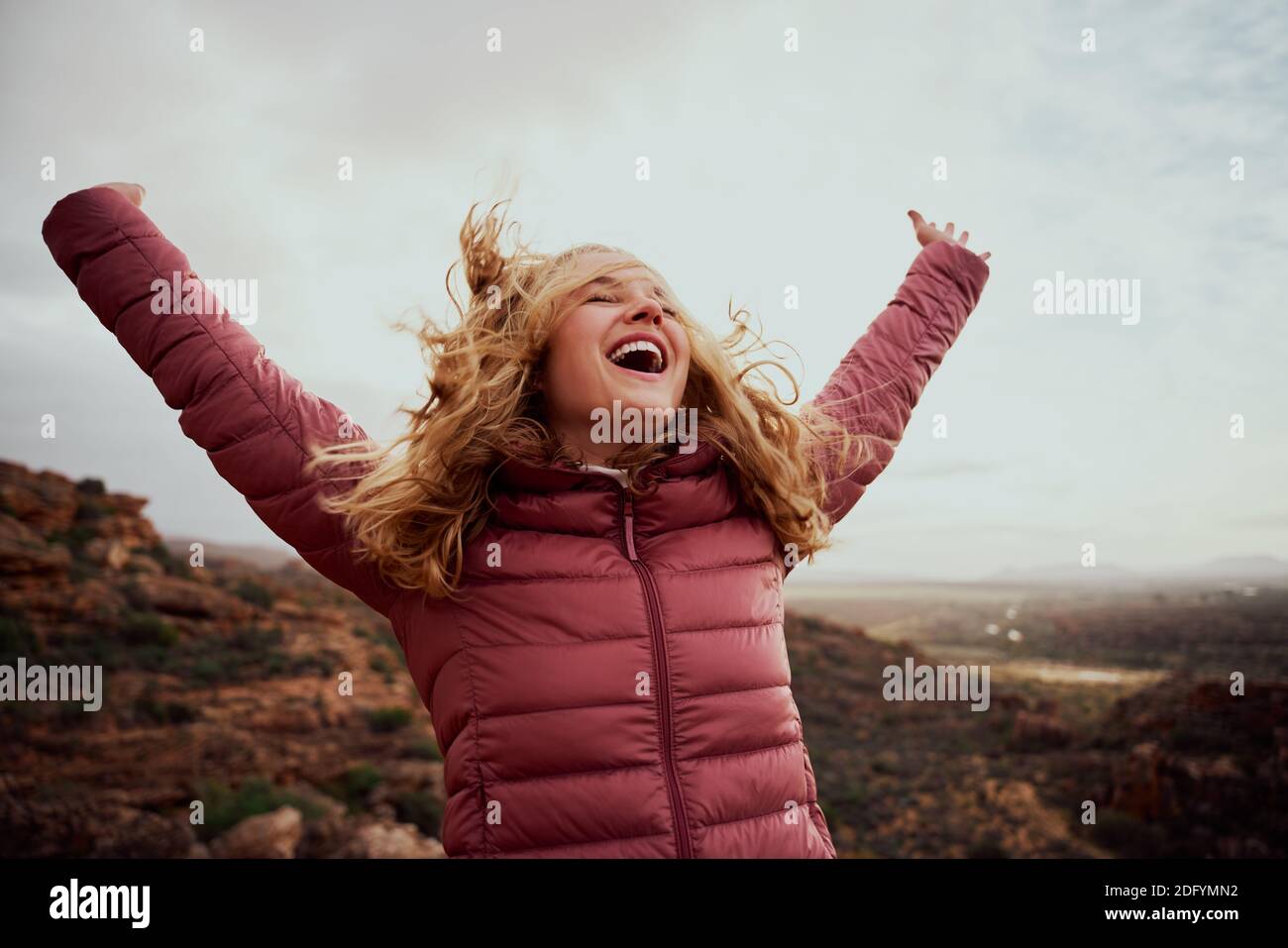 Cheerful young woman with hands raised and outstretched mountaineer with hair flying in wind enjoying fresh breeze - happiness and travel - achieving Stock Photo