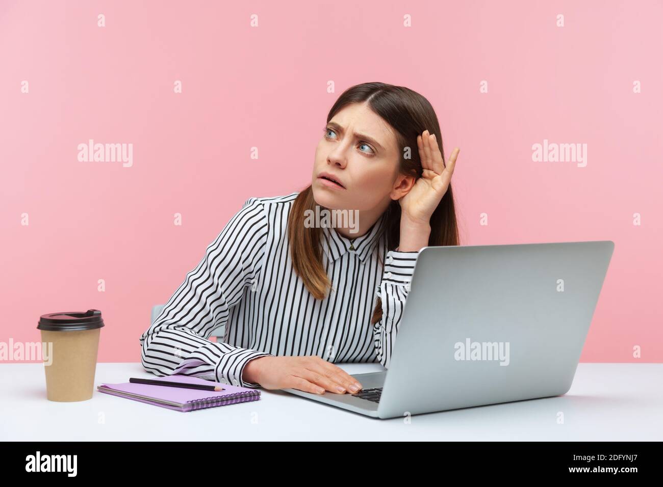 I can't hear you. Business woman holding arm near ear trying to listen secret talk on video call on laptop, bad internet connection, online conference Stock Photo