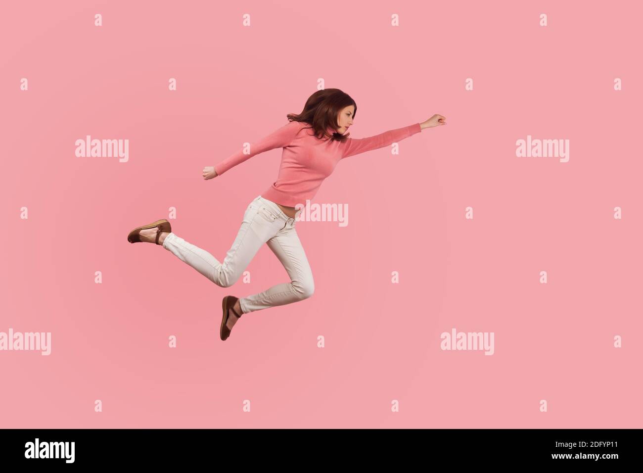 Confident purposeful brunette woman flying in air like superhero, ready to cope with problems and difficulties. Indoor studio shot isolated on pink ba Stock Photo