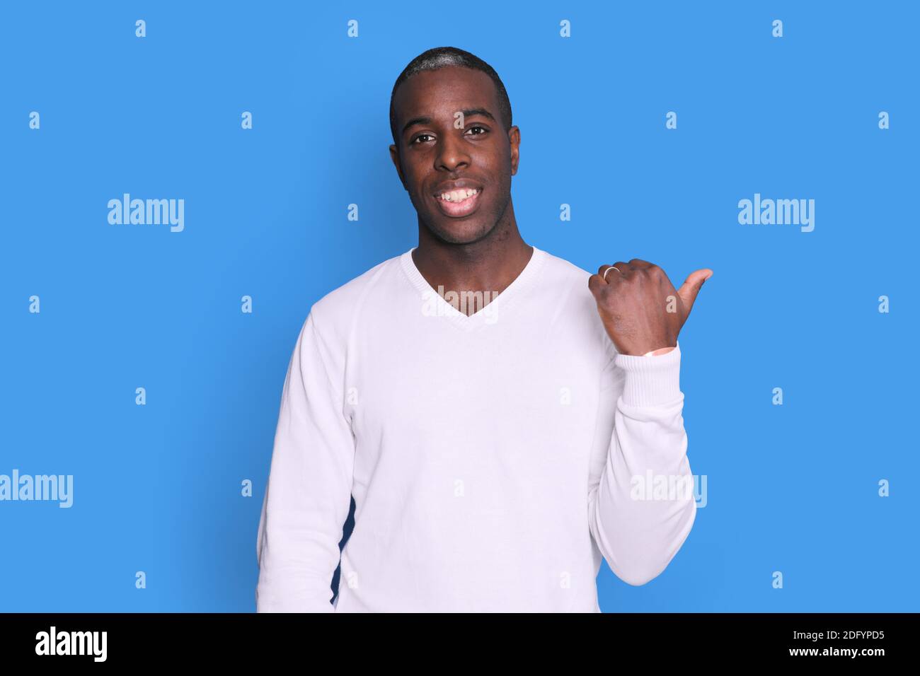 Black smiling Guy Pointing Thumb Aside At Blank Space For Text Standing On Blue Studio Background. Stock Photo