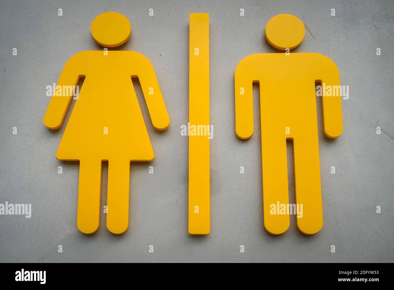 Yellow side by side woman and man symbols of public toilet restroom sign on a concrete wall Stock Photo