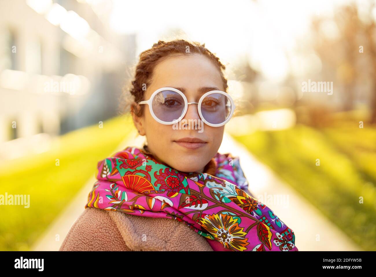 Portrait of young woman wearing warm coat, colorful scarf and sunglasses during winter Stock Photo