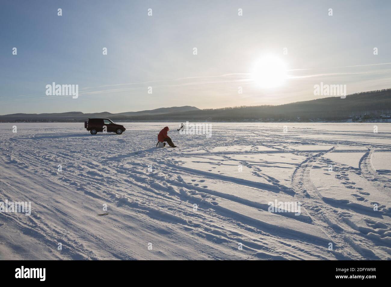 Fishermen catch fish on a snowy lake, in the evening light. Stock Photo