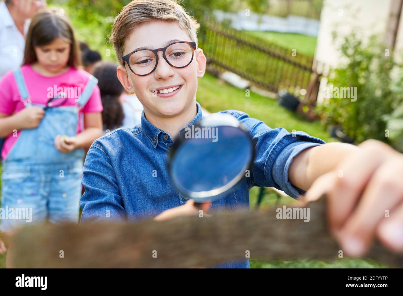 Boy curiously examines a piece of tree bark with a magnifying glass in