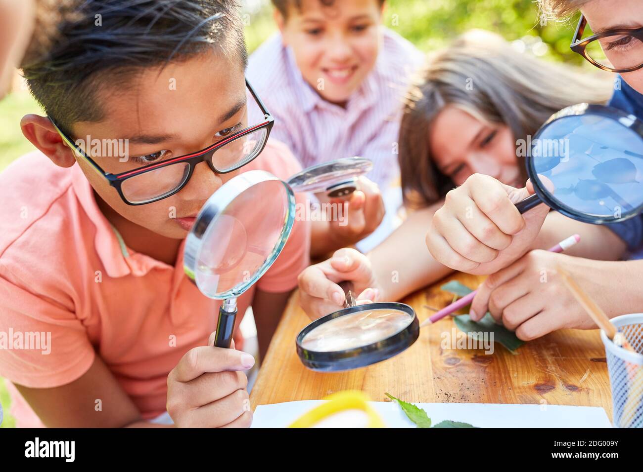 Children in ecological holiday course curiously look at leaf through magnifying glass at summer camp Stock Photo
