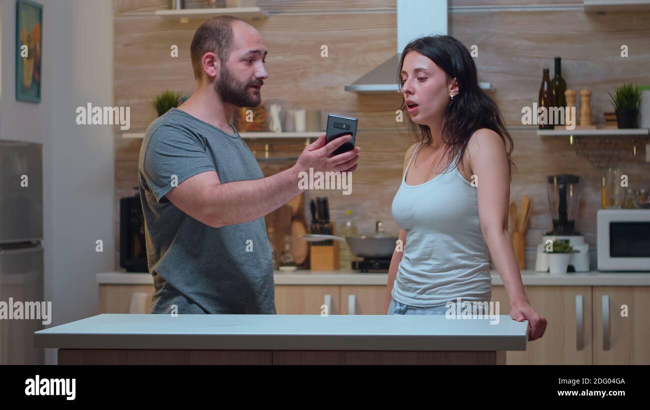 Angry partner asking explanations for messages. Jealous man cheated angry frustrated offended irritated accusing woman of infidelity arguing her with photos from smartphone screaming desperate Stock Photo