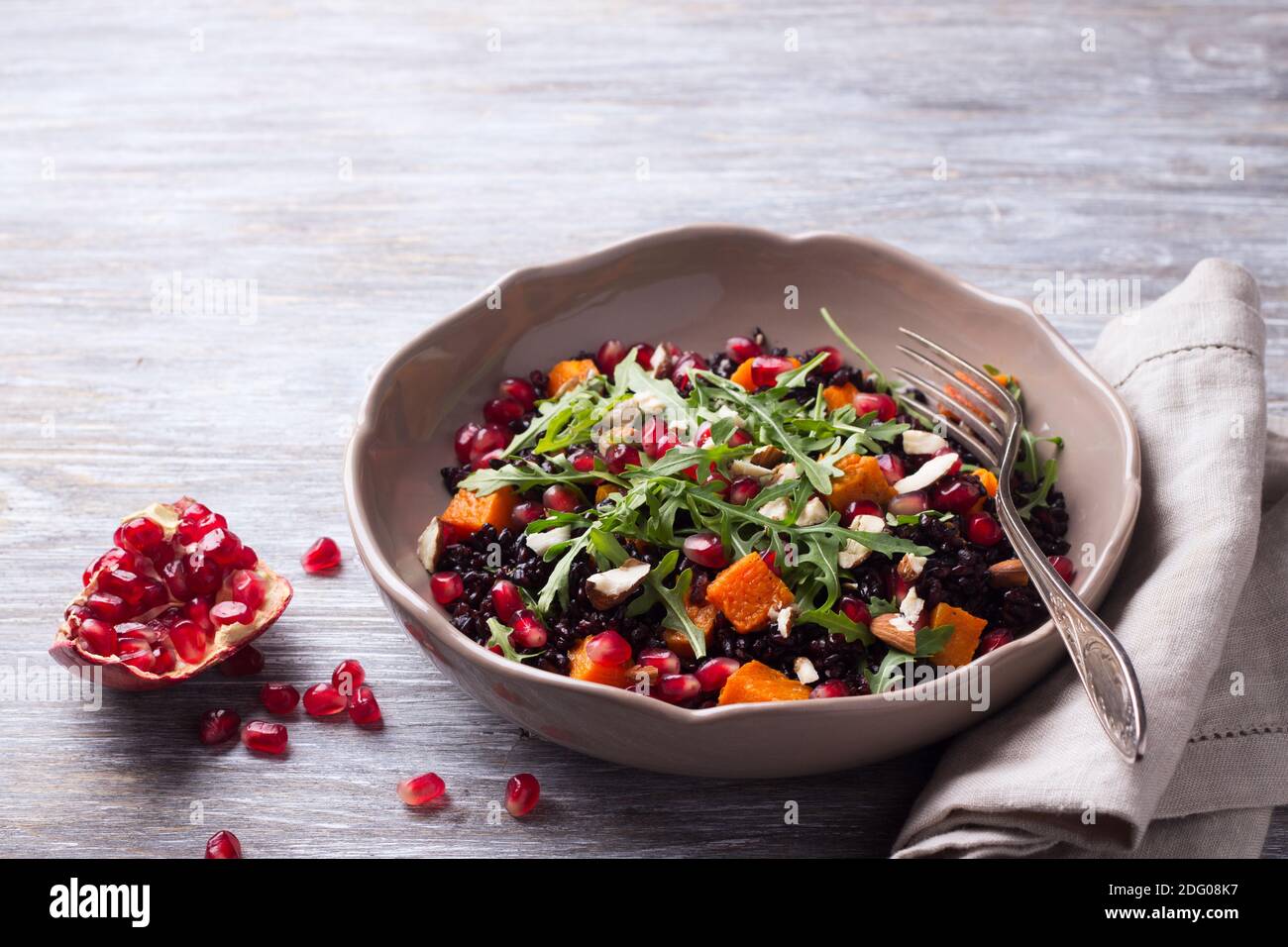 Salad with black rice, baked pumpkin, pomegranate seeds, arugula and nuts on a gray background. Delicious vegan food Stock Photo