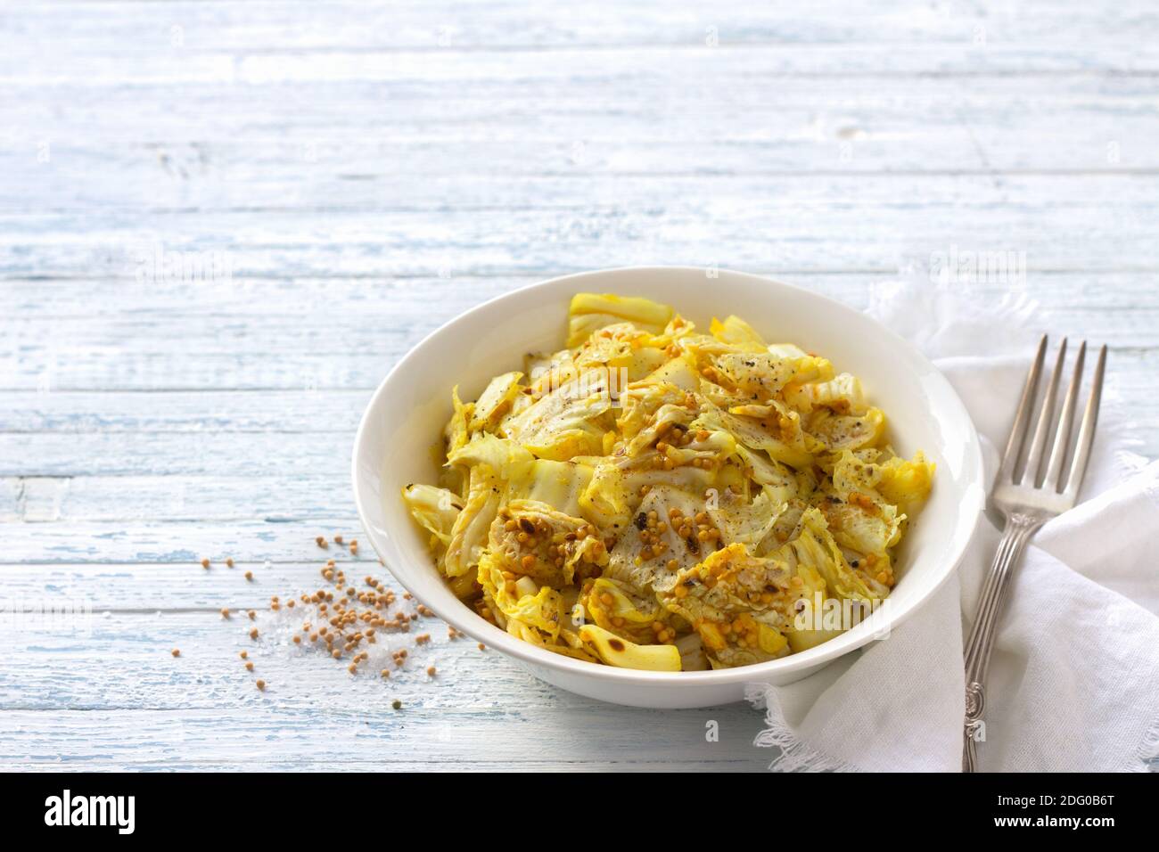 Pickled chinese cabbage with garlic and spices, mustard, turmeric, hot pepper in a white bowl on a blue background, selective focus, free space. Healt Stock Photo