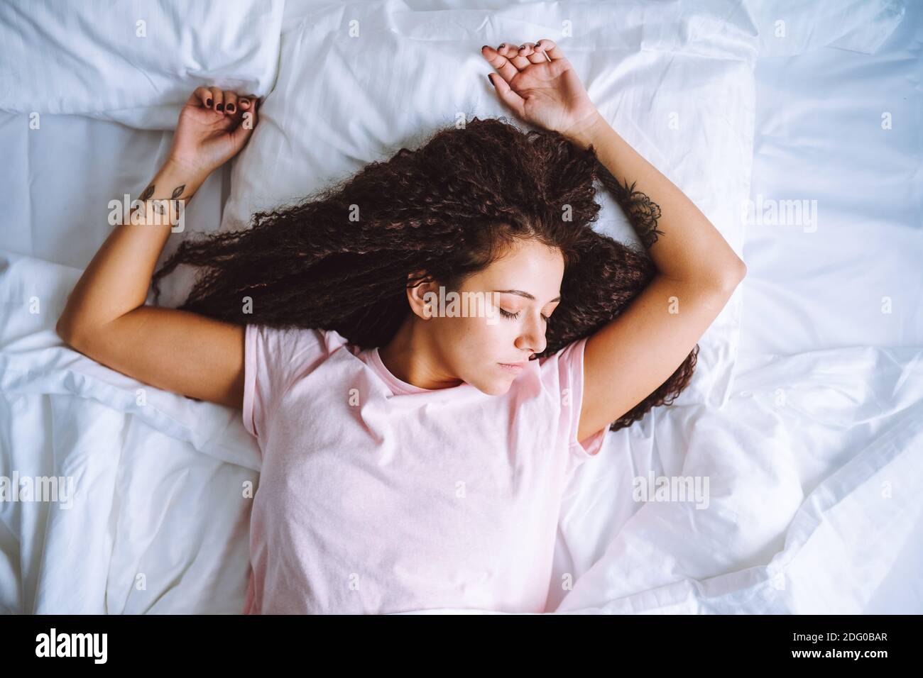 Top view of young afro haired woman sleeping in morning lying on bed with snow white linens. Stock Photo