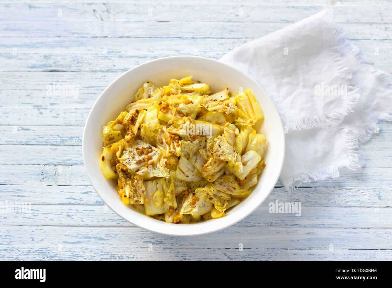 Pickled chinese cabbage with garlic and spices, mustard, turmeric, hot pepper in a white bowl on a blue background, selective focus, top view. Healthy Stock Photo