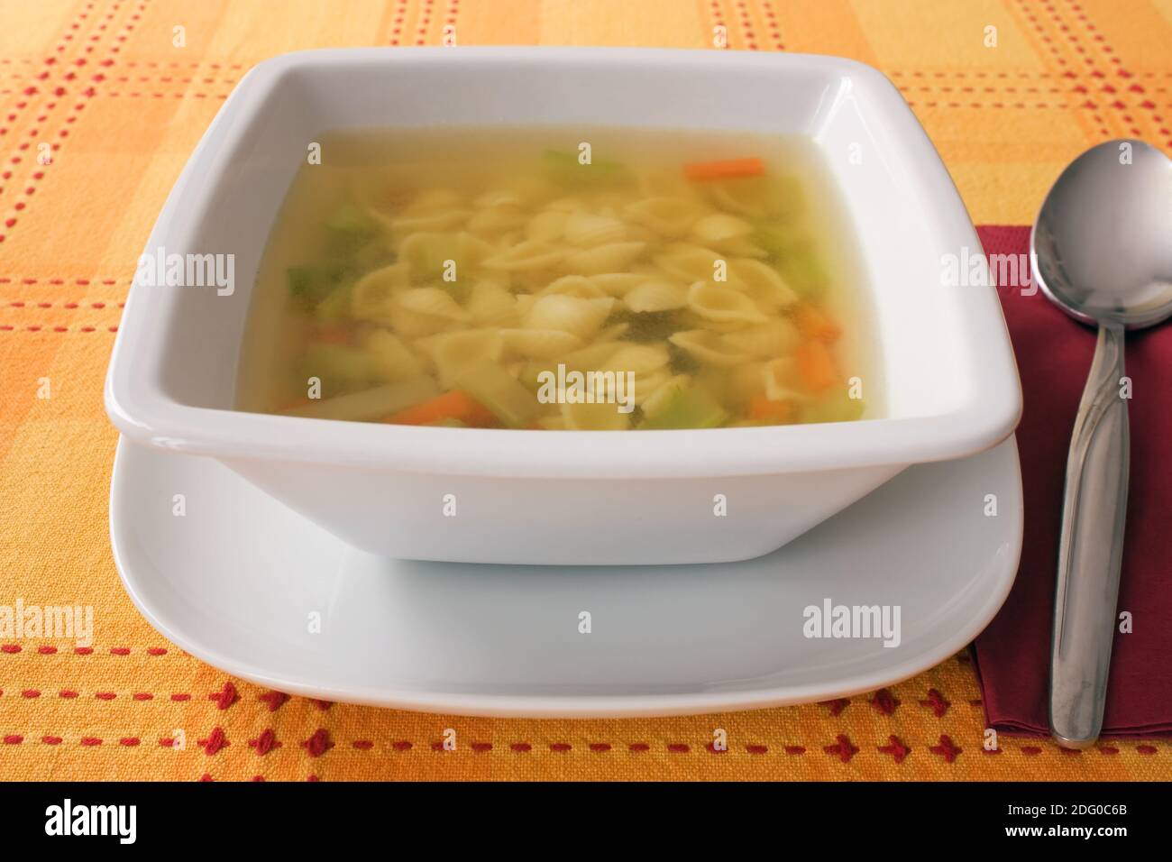 Aufnahme mit geringer TiefenschÃ¤rfe einer GemÃ¼sesuppe mit Nudeln auf einer orangen Tischdecke. Stock Photo