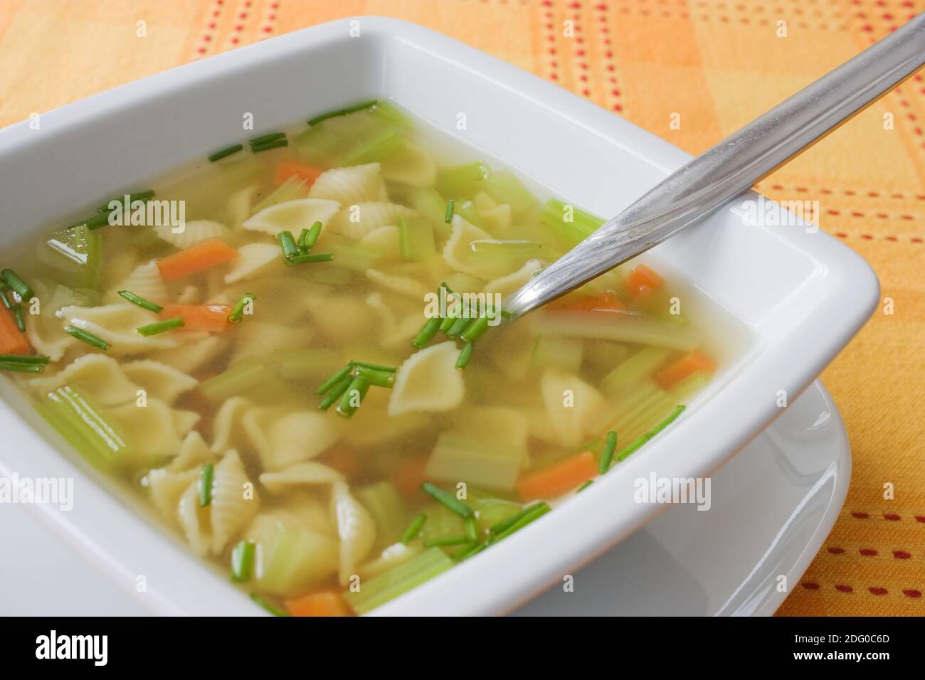 Aufnahme mit geringer TiefenschÃ¤rfe einer GemÃ¼sesuppe mit Nudeln auf einer orangen Tischdecke. Stock Photo