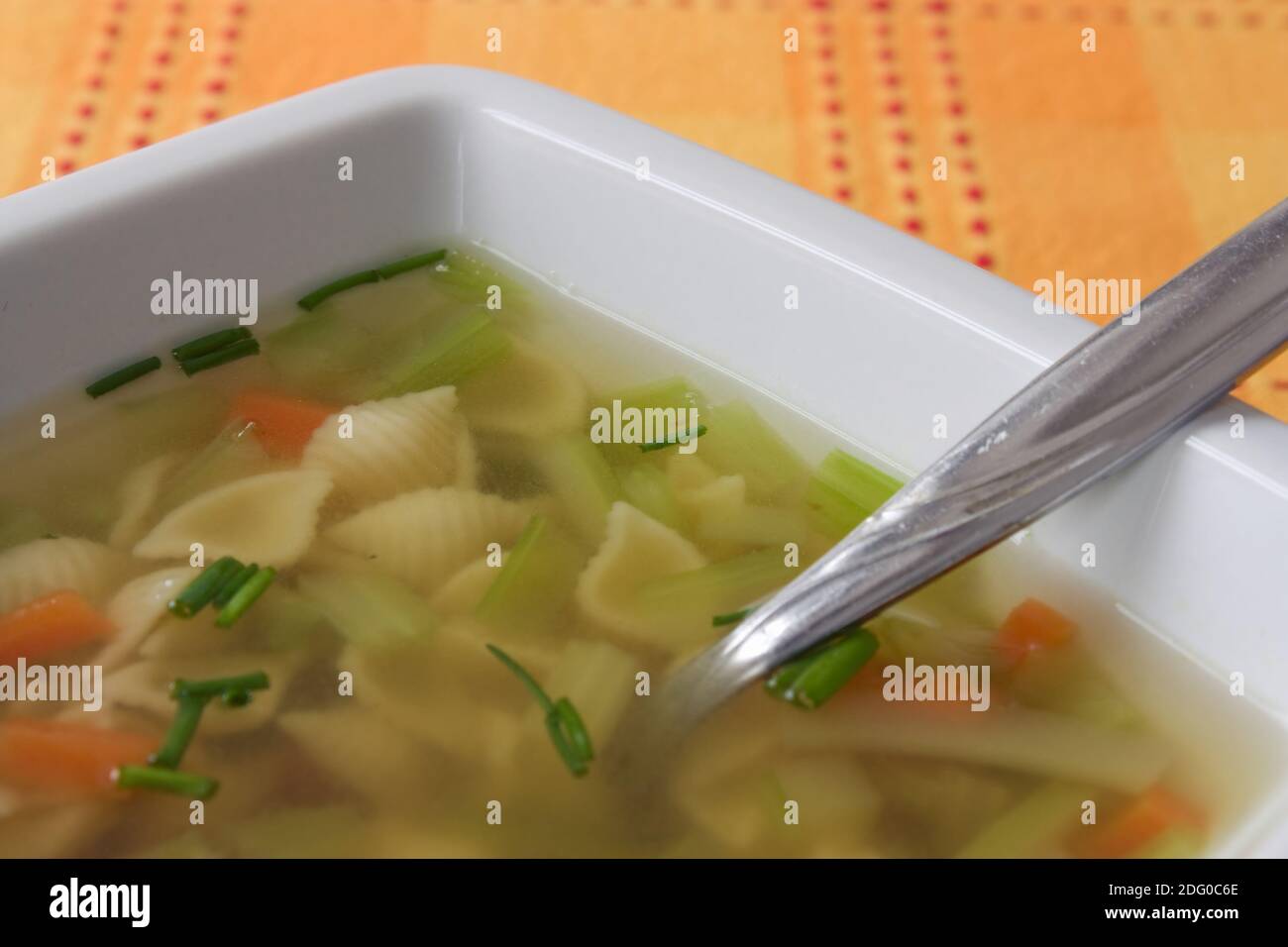 Aufnahme mit geringer TiefenschÃ¤rfe einer GemÃ¼sesuppe mit Nudeln auf einer orangen Tischdecke. Stock Photo