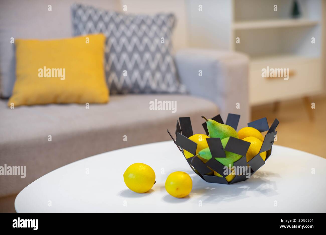 Close-up of decorative bowl with fruits on white table. Lemons and pears. Modern interior. Stock Photo