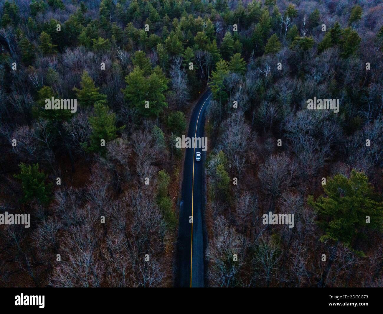 An aerial view of a white car driving down a wet asphalt road through ...