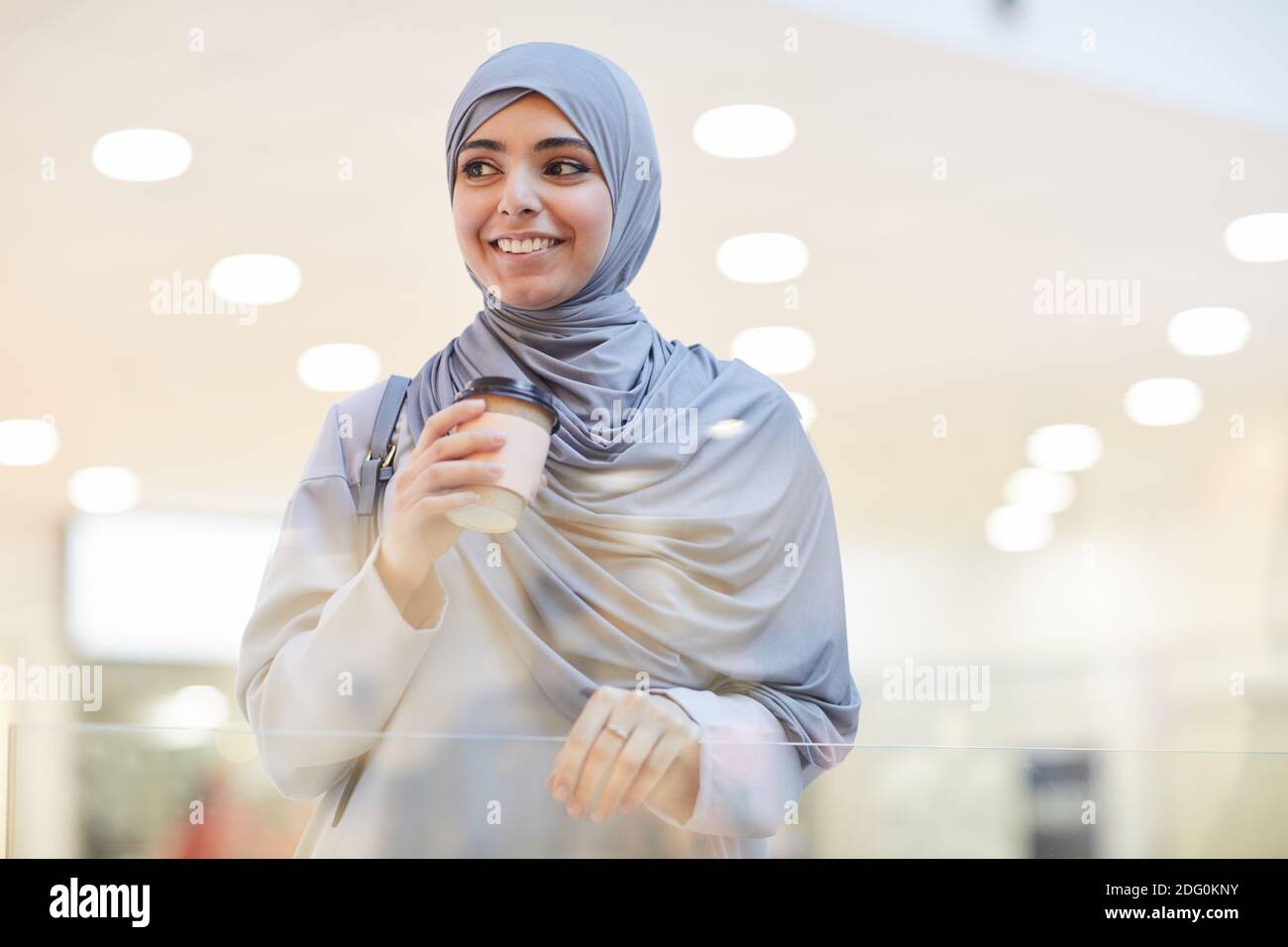 Waist up portrait of young Middle-Eastern woman wearing headscarf and holding coffee cup while enjoying shopping in city, copy space Stock Photo