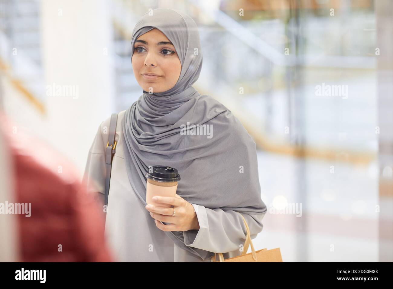 Waist up portrait of young Middle-Eastern woman wearing headscarf and looking at window displays while enjoying shopping in mall, copy space Stock Photo