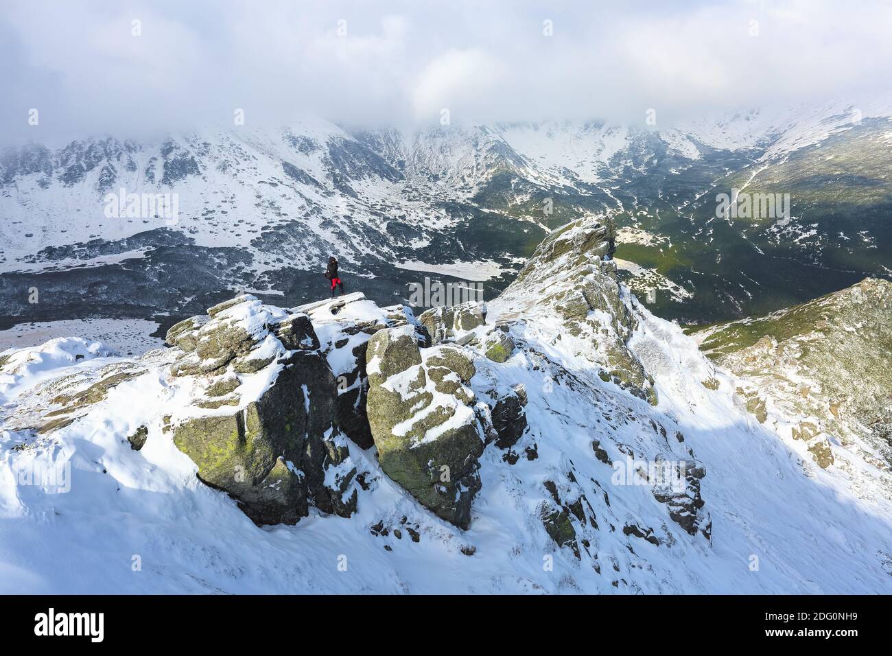 Landscape on the cold winter morning. Happy tourist in sport clothes is standing at the edge of the precipice. High mountains with snow white peaks. S Stock Photo