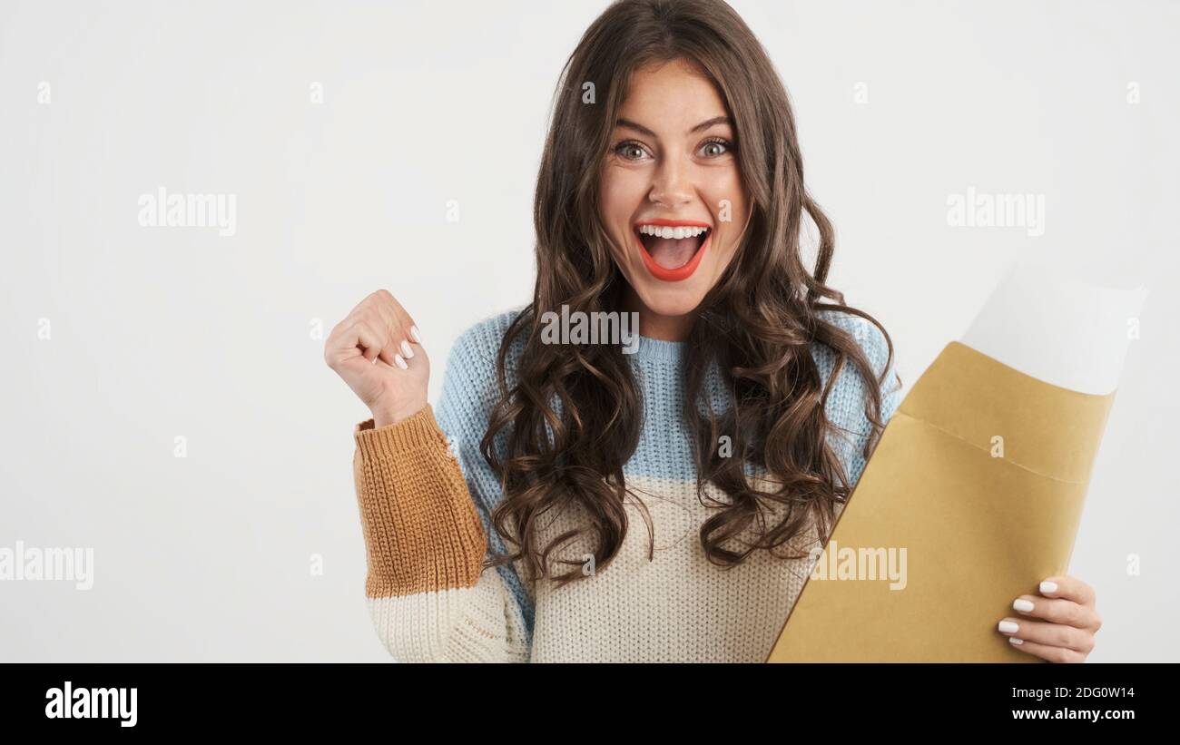 Pretty excited girl in sweater opening envelope with exam results and happily rejoicing on camera isolated Stock Photo