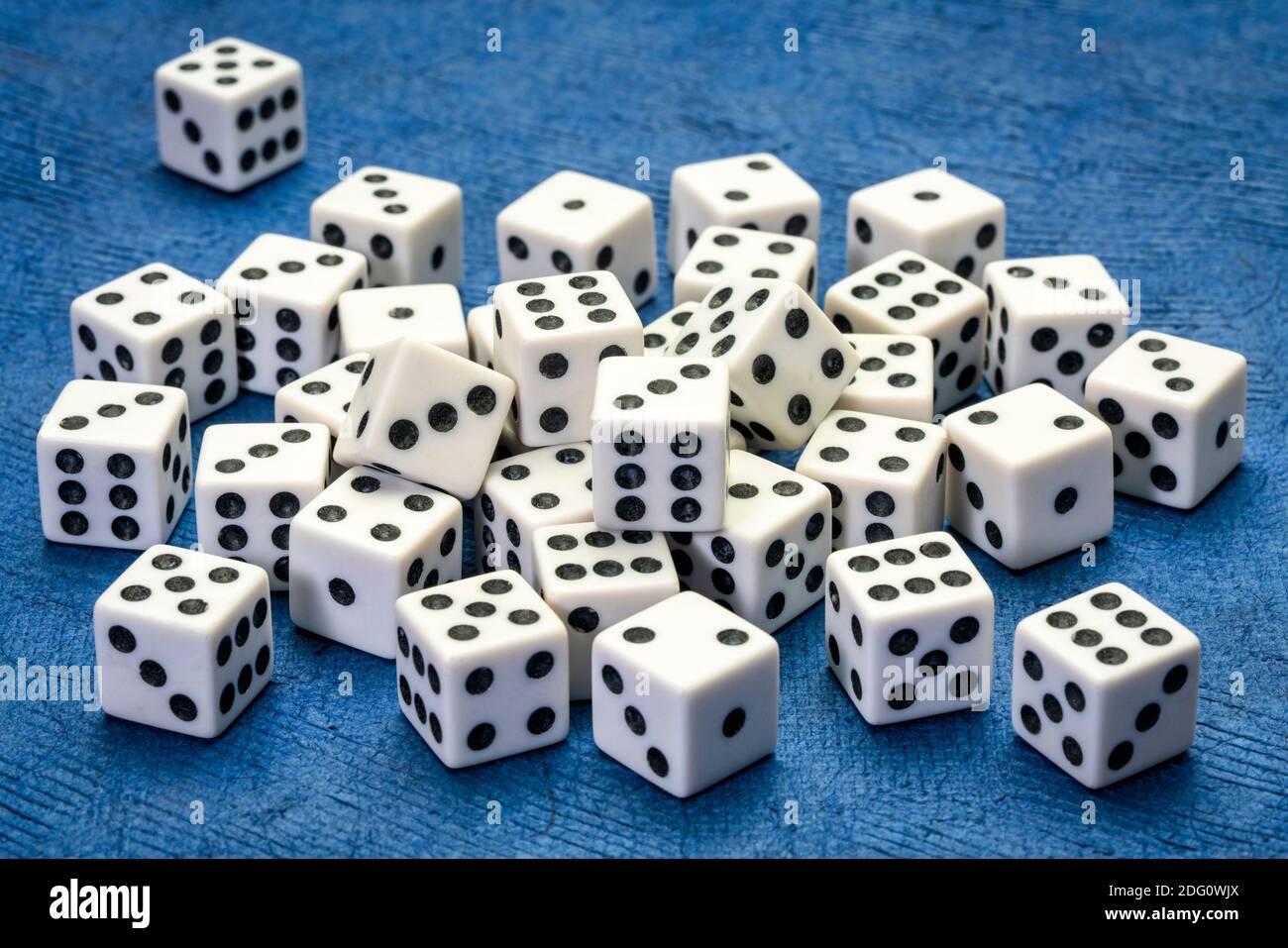 pile of white cubic dice with black pips (dots) against blue handmade paper, game, gamble, chance and risk concept Stock Photo