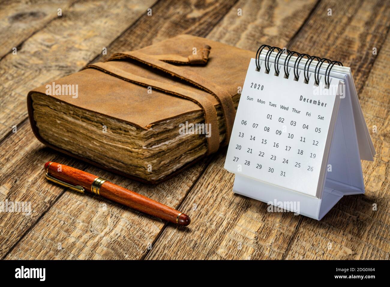 December 2020 - spiral desktop calendar against rustic wood with an antique leather-bound journal and a stylish pen, season,  time and business concep Stock Photo