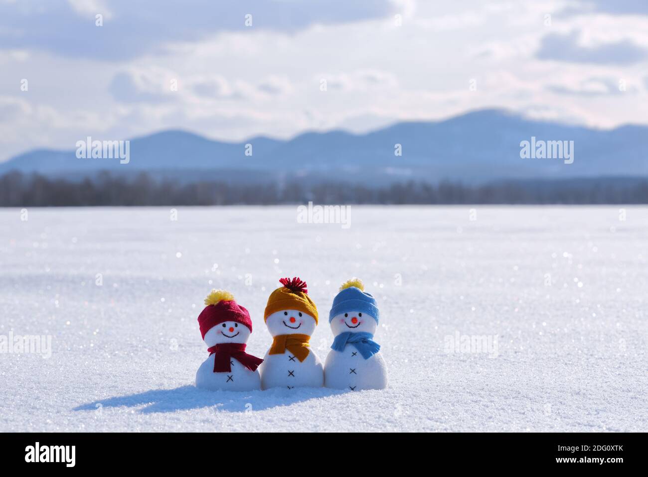 Snowman in hat and scalf on snowy field. Beautiful winter background. Merry christmas and happy new year. Landscape with high mountains. Stock Photo