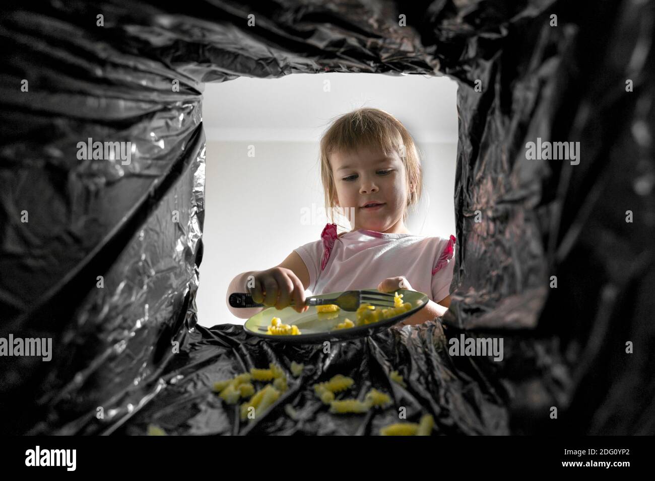 child throws pasta into the trash bin. view from the trash can. excessive consumption Stock Photo