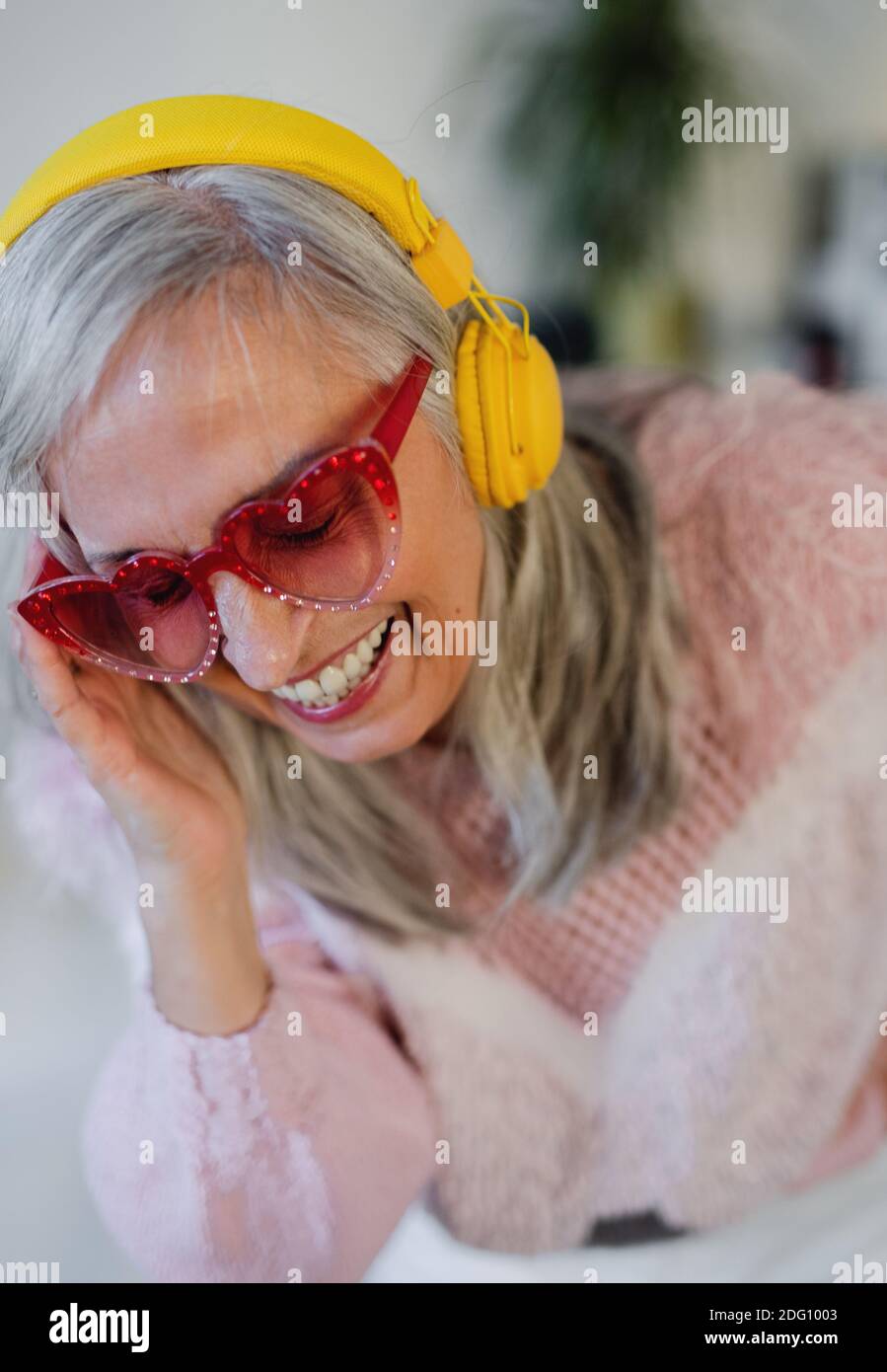 Portrait of senior woman with sunglasses and headphones indoors at home, laughing. Stock Photo