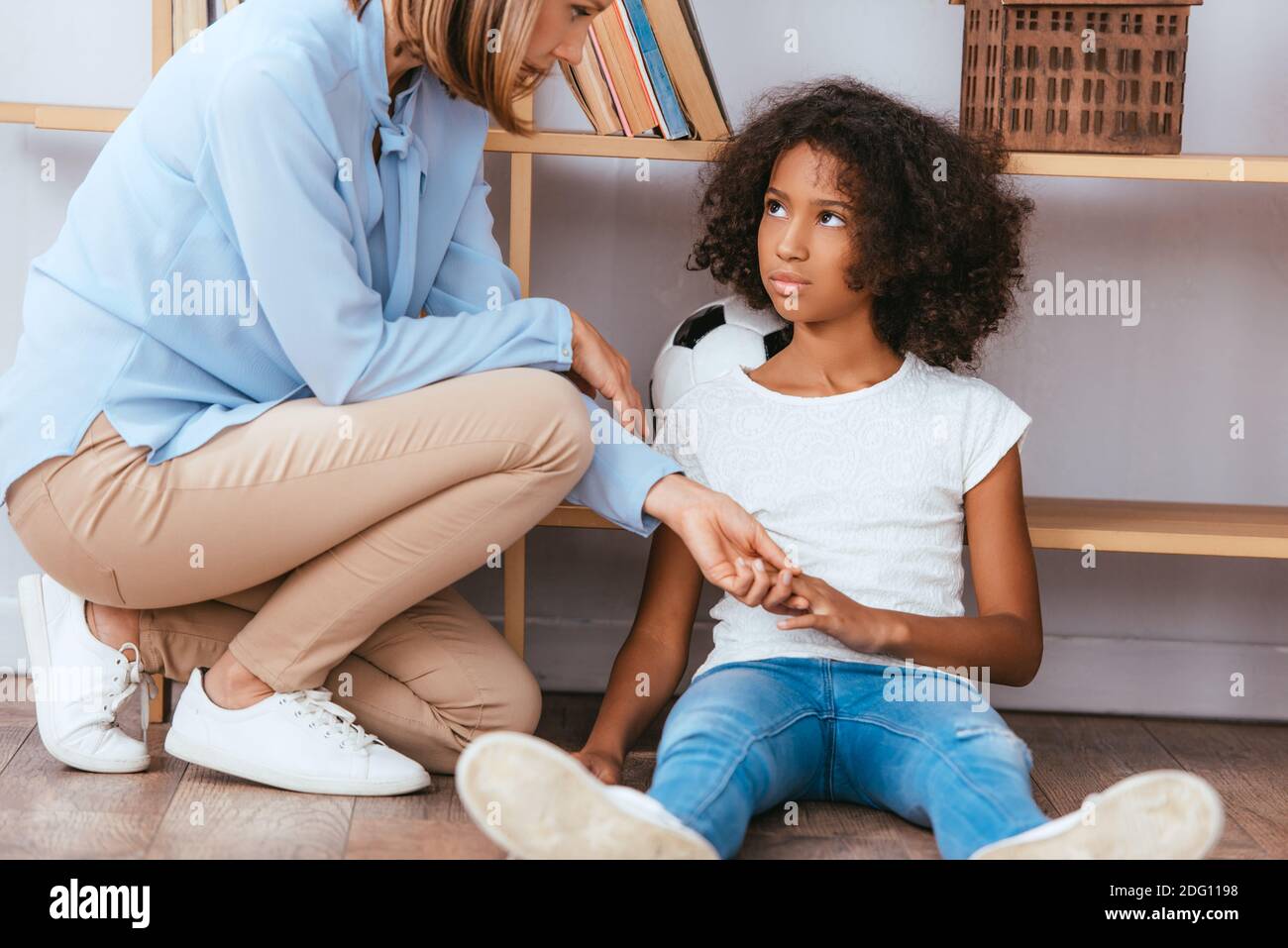 Psychologist holding hands with upset african american girl with autism