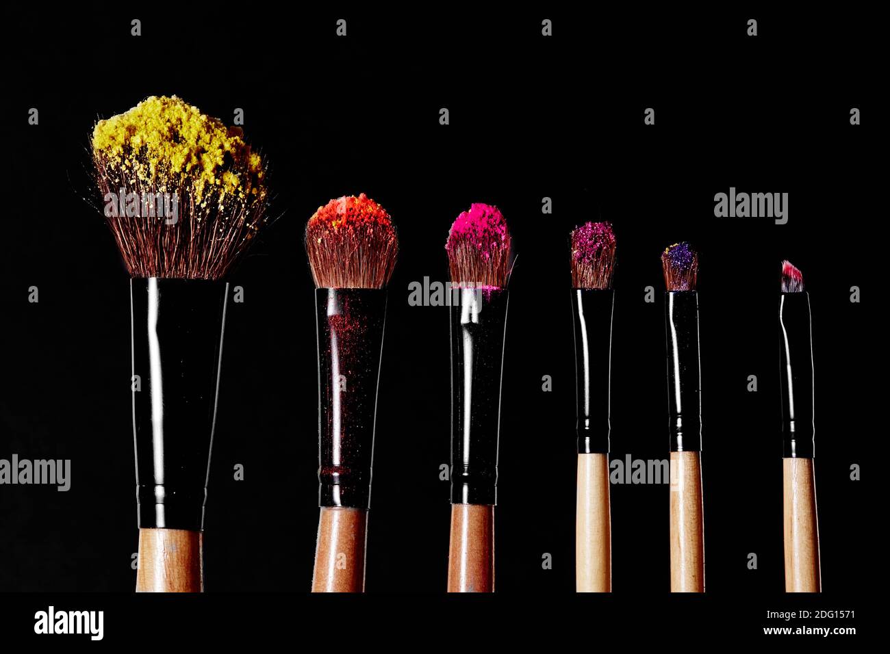 Make-up tools. Brush for makeup. Cosmetic brushes on black with bright dust splash. Colorful shadows pigment. Stock Photo