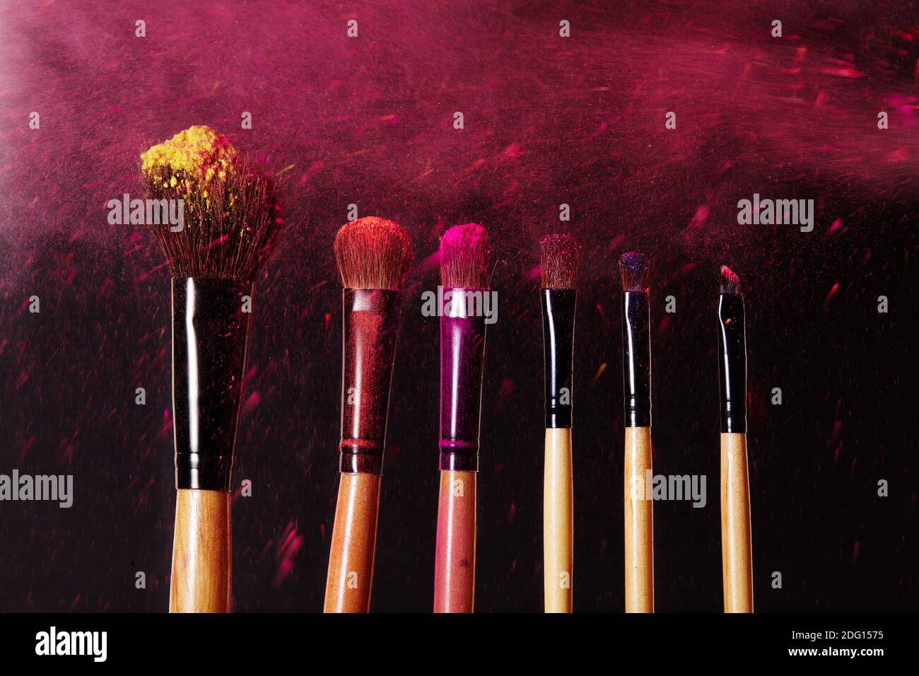 Make-up tools. Brush for makeup. Cosmetic brushes on black with bright dust splash. Colorful pink shadows pigment. Stock Photo