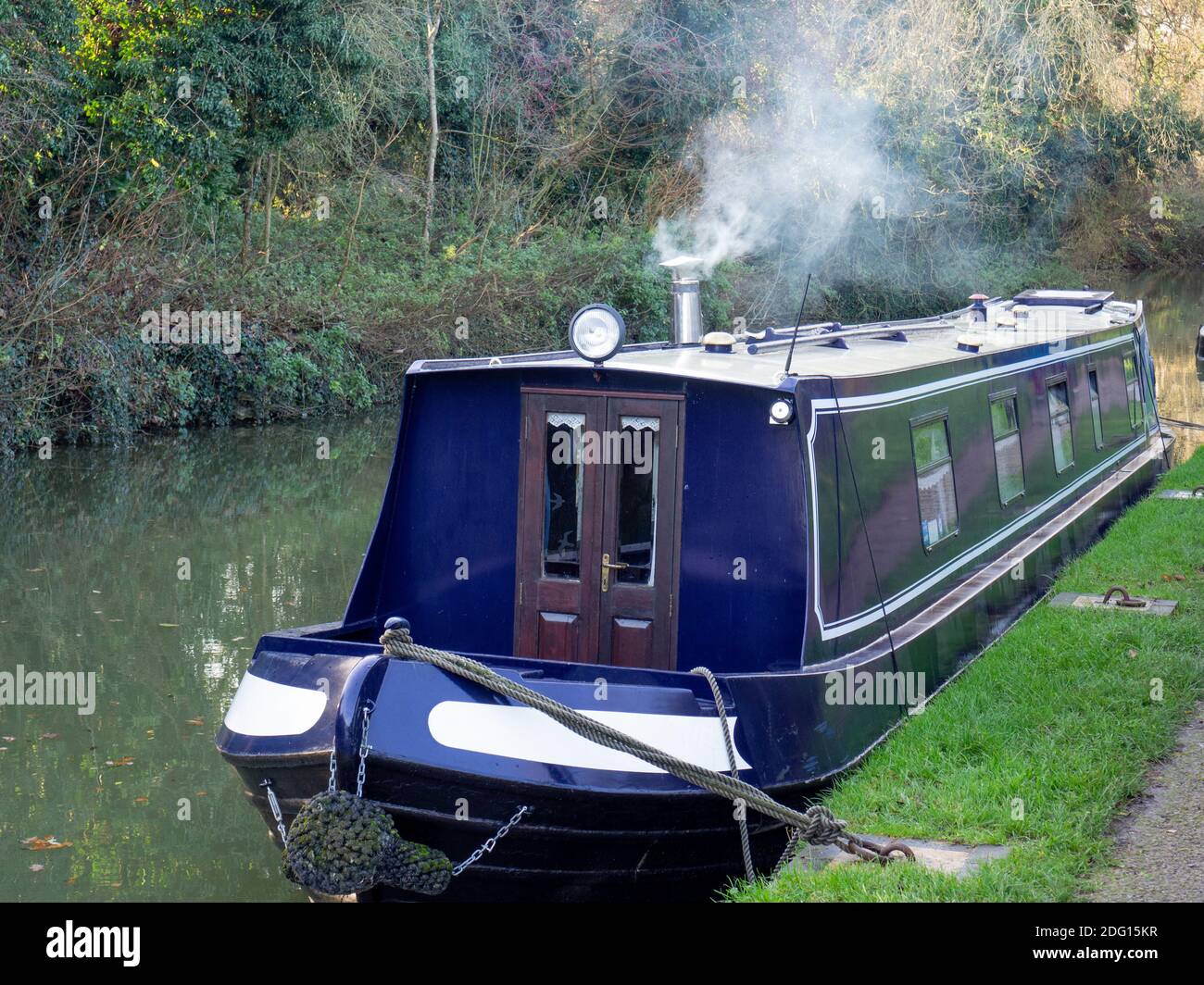 Winter scene on the Grand Union canal at Stoke Bruerne, Northamptonshire, UK; moored narrowboat with smoke coming from the chimney Stock Photo