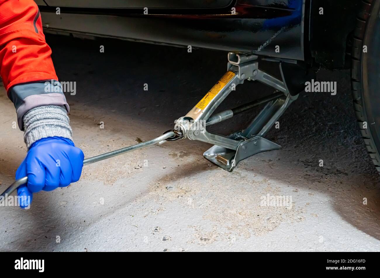 Arm and hand of a person raising a car on its emergency jack stand