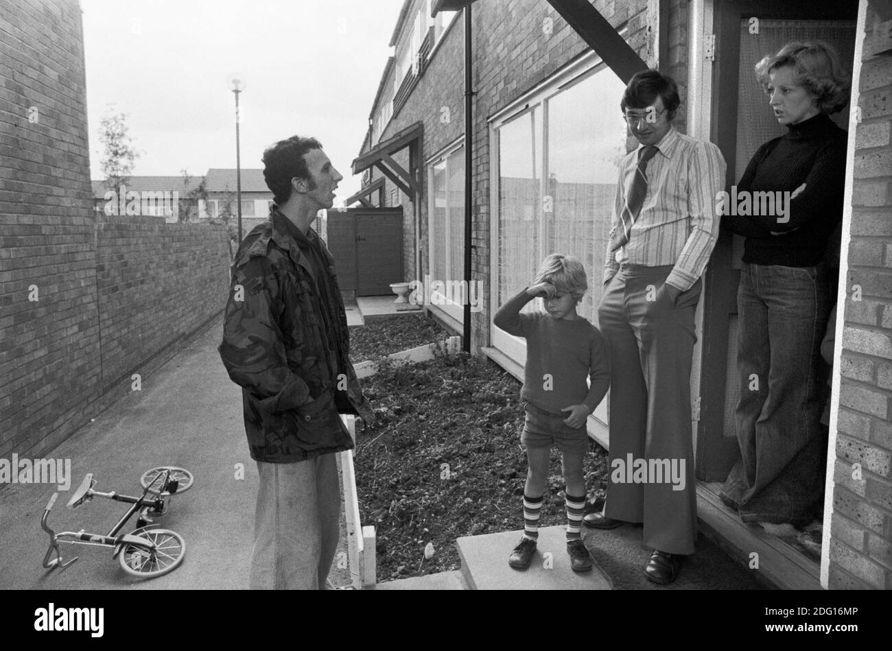 1970s family, middle income professional couple, mother, father and child, they have come to the front door to chat to a neighbour. Standing on the front door step. 1977 Modern housing development in new town England 1977 HOMER SYKES Stock Photo