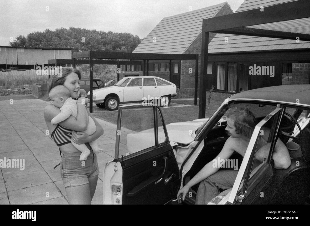 1970s UK, professional middle income couple outside their new modern home on a recently built new housing estate, a modern development. Hanging out with the new baby in arms by their car that is parked out side their home 1977 England. Milton Keynes Buckinghamshire HOMER SYKES Stock Photo