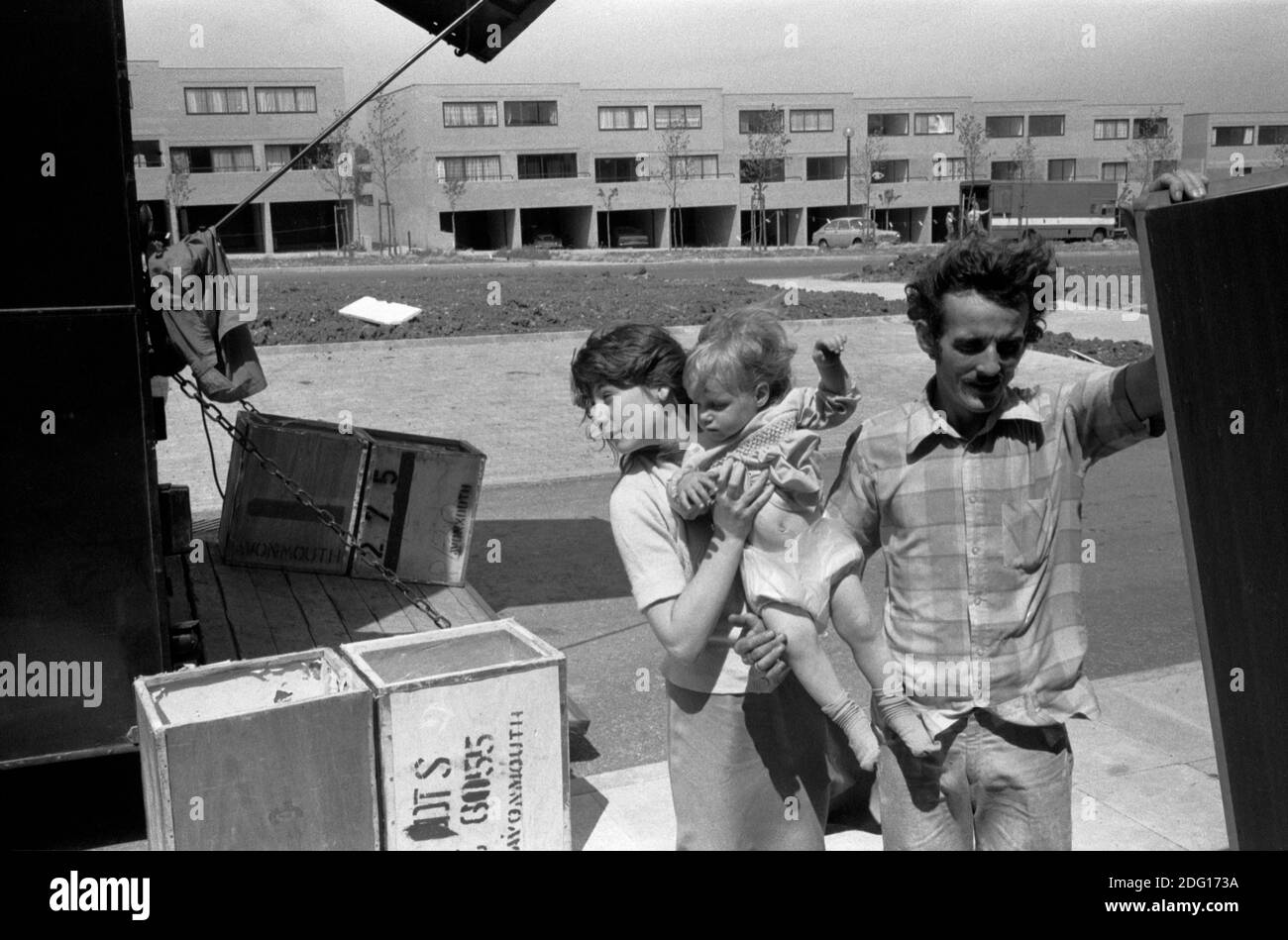 Moving house, family move into new home on a new estate1970s .Father and oldest daughter who is carrying her baby sister. Packing cases, old tea chests coming off the removal van. 1977 Milton Keynes Buckinghamshire UK HOMER SYKES Stock Photo