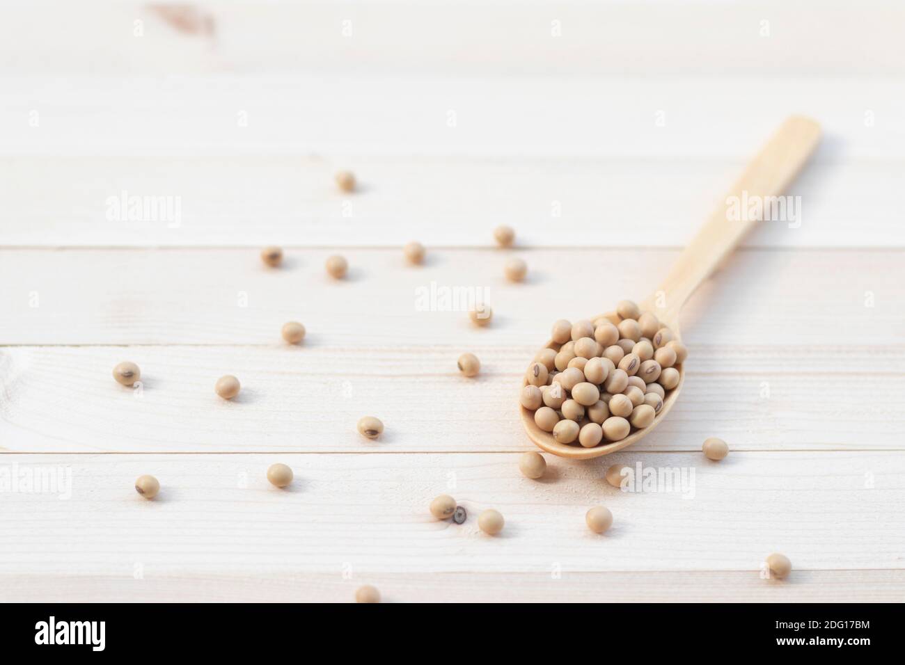 Soybean seeds on a wooden spoon with light pine wood background. Stock Photo