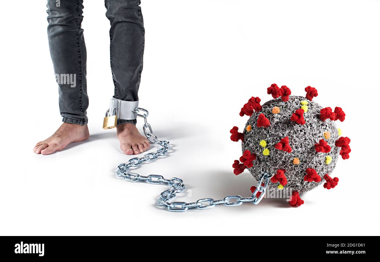 A man is chained to his foot with the coronavirus. Covid 19 chains us like a ball and chain. Stock Photo