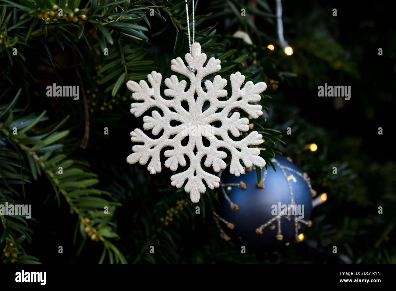 snowflake ornament and christmas tree ball hanging outside in yew tree Stock Photo