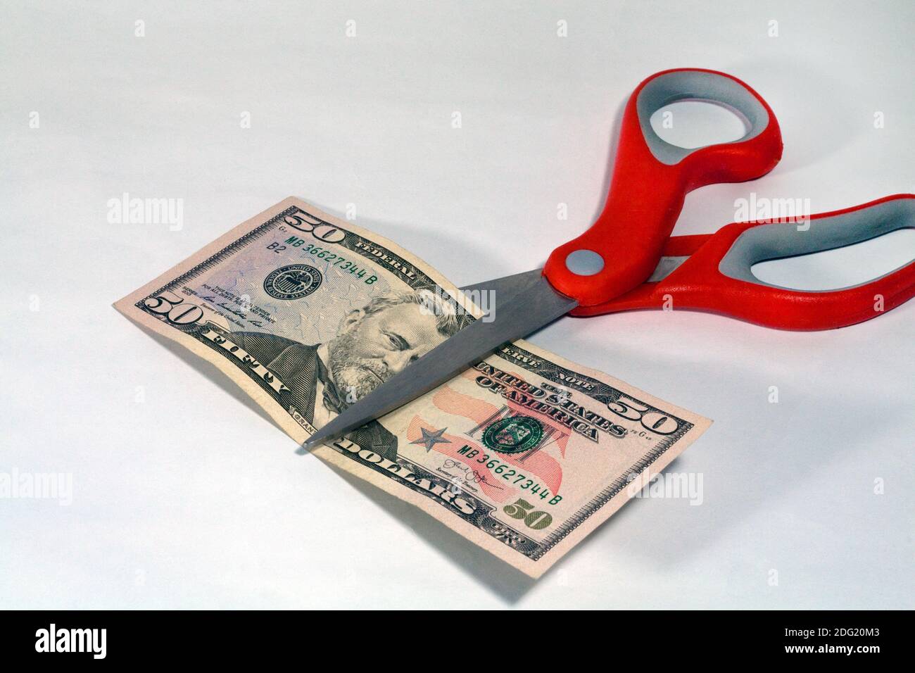 A pair of red-handled scissors cutting a U.S. 50 dollar bill in half. Stock Photo