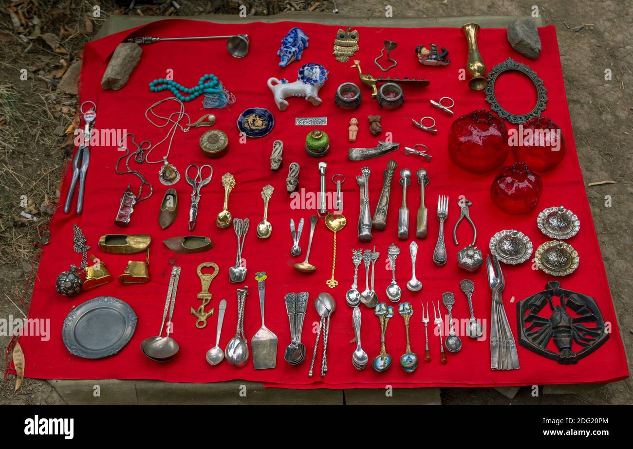 Tbilisi, Georgia - July 20, 2019: vintage crockery and accessories – tea spoons, forks, ashtrays laid out on a red cloth for sale at flea market Stock Photo