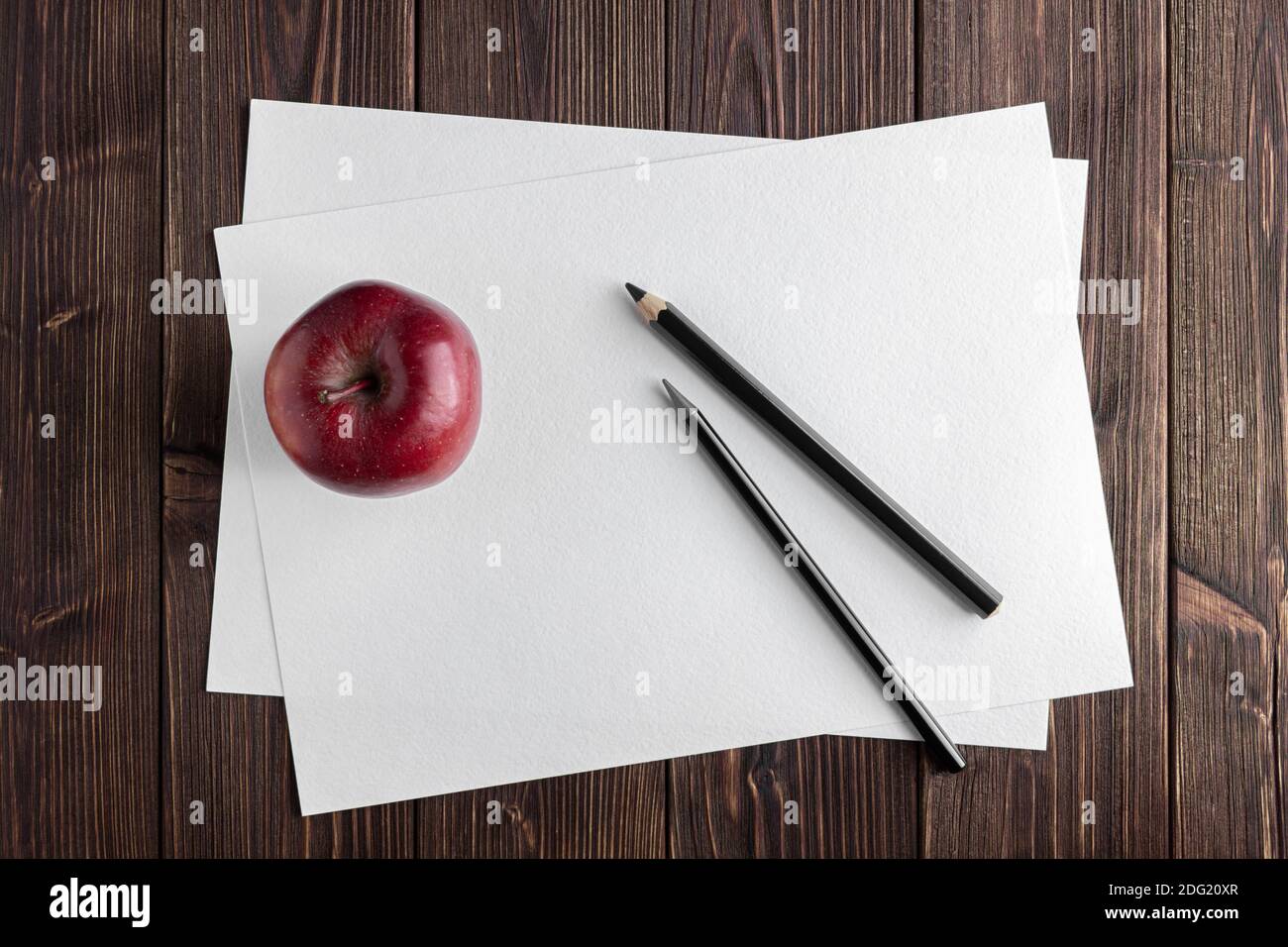 Watercolor papers with red apple on wooden table. Top view of fresh fruit. Stock Photo