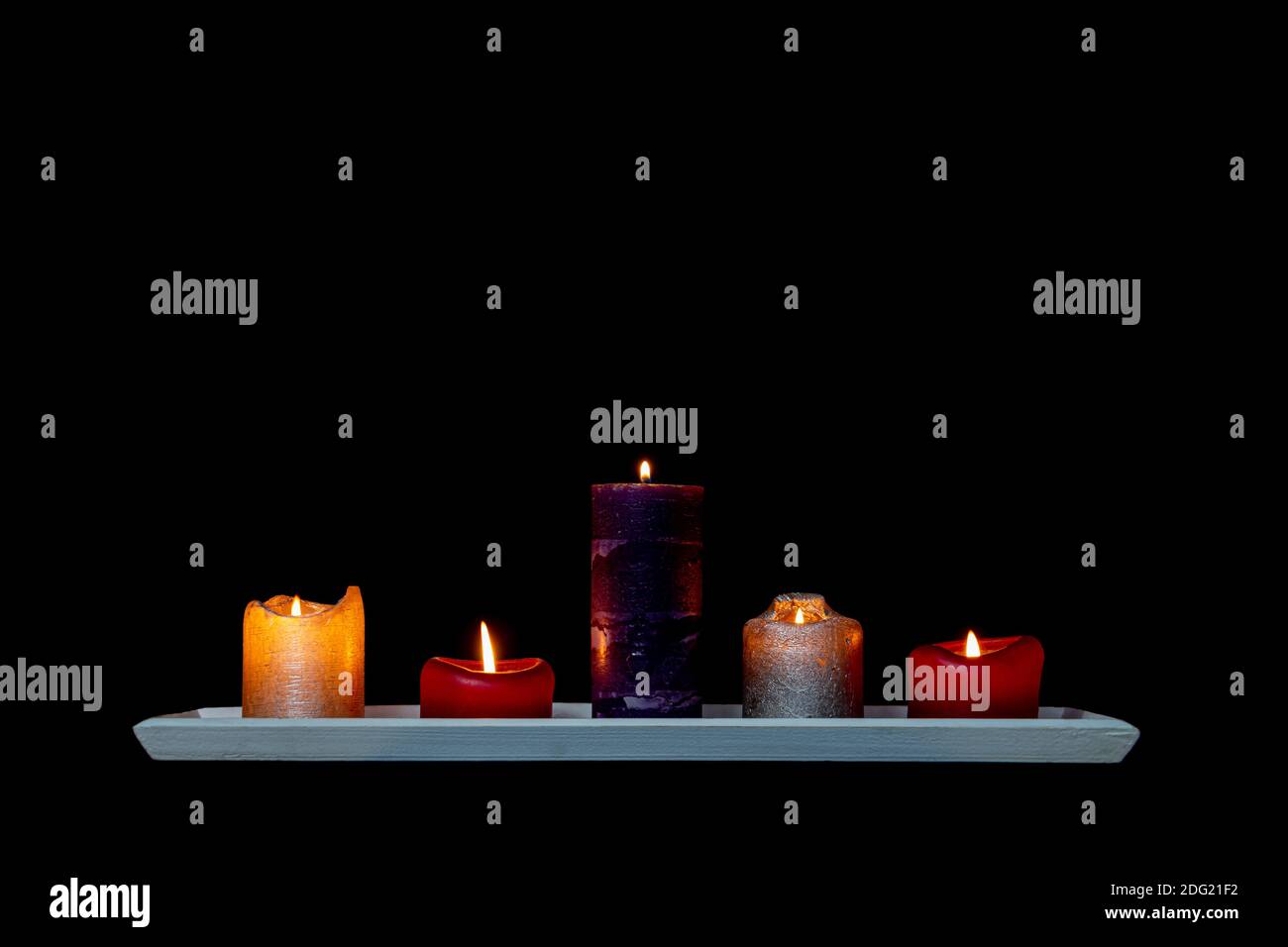 Colorful candles on a wooden shelf isolated on black background with copy space Stock Photo