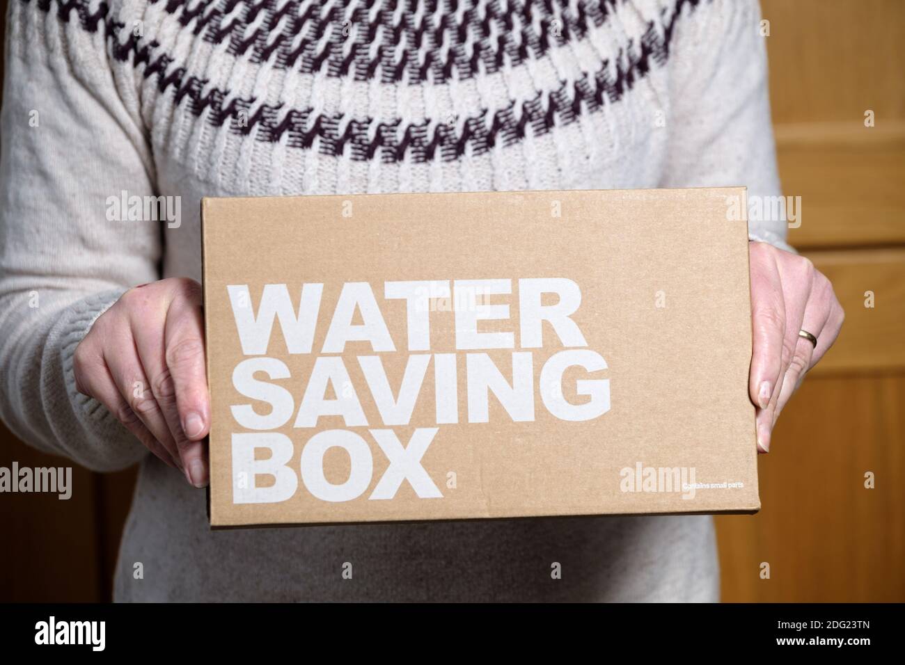 A customer is shown holding a box containing water saving pack supplied by a consumers local water authority. The box contains water saving devices Stock Photo