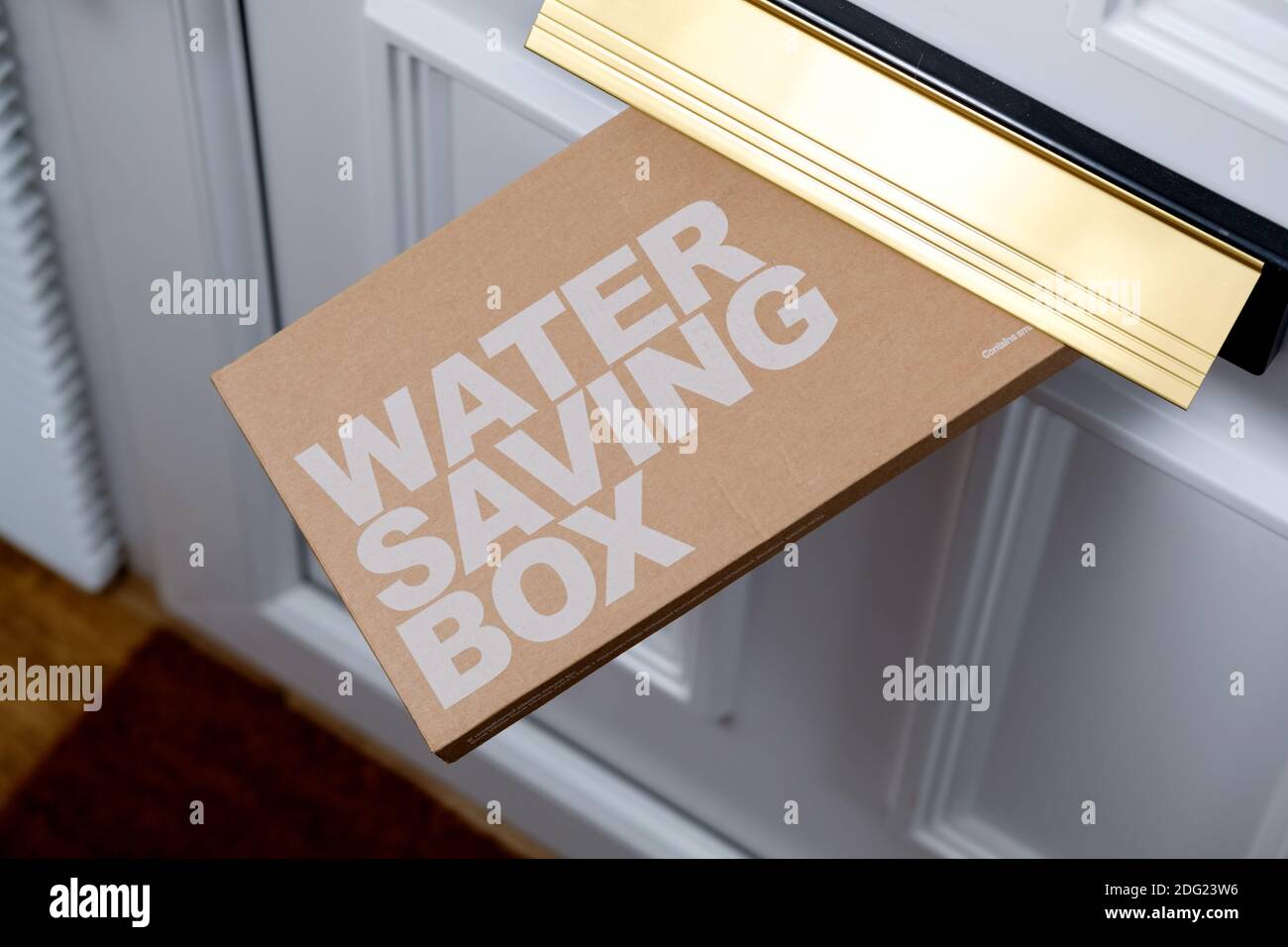A box containing water saving pack supplied by a customers local water authority is shown being posted through the consumers front door Stock Photo