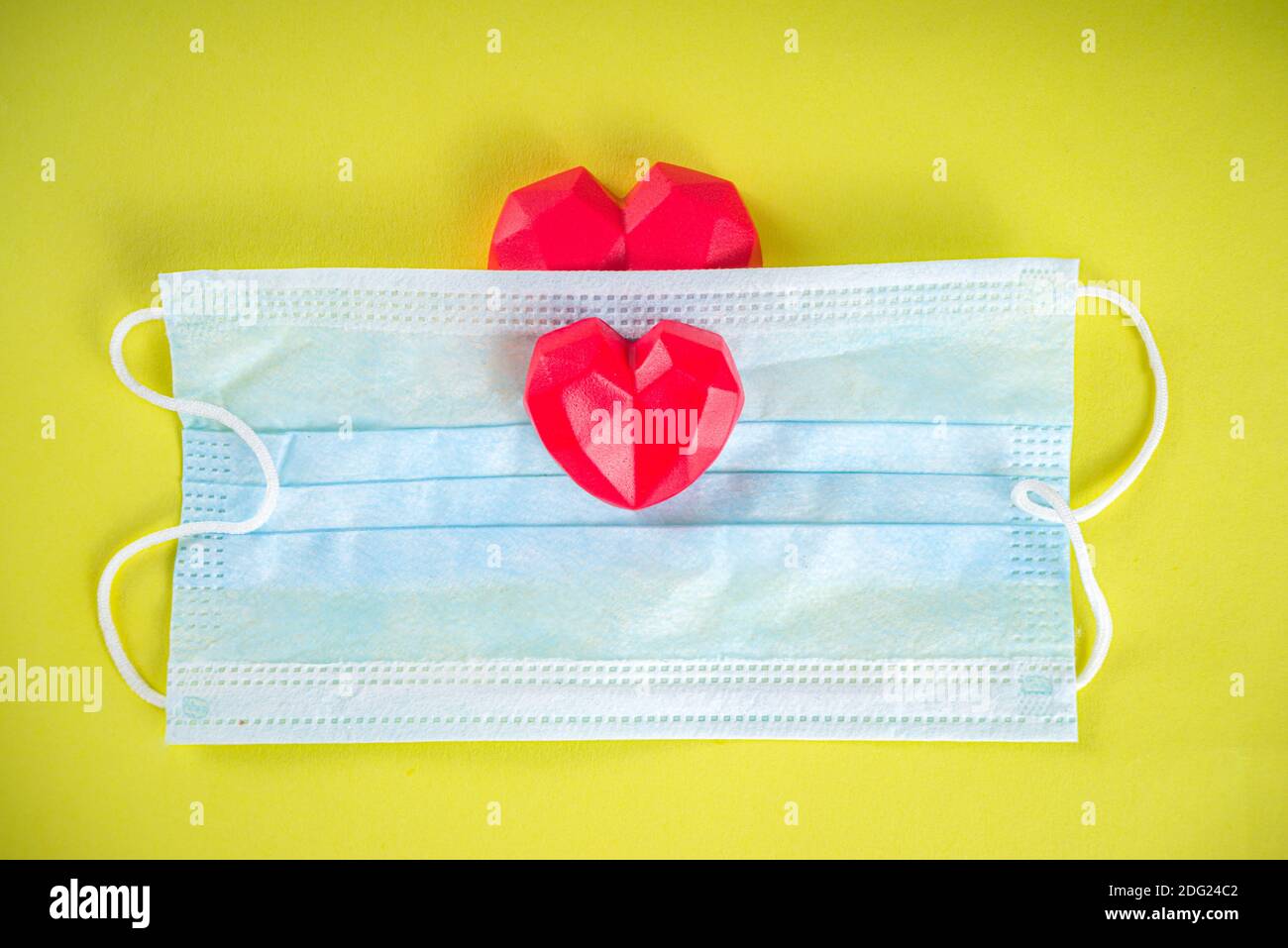 Red heart with medical mask, Valentine day or heath care, body renovation, protection concept, flatlay on bright yellow background. Complication of ca Stock Photo