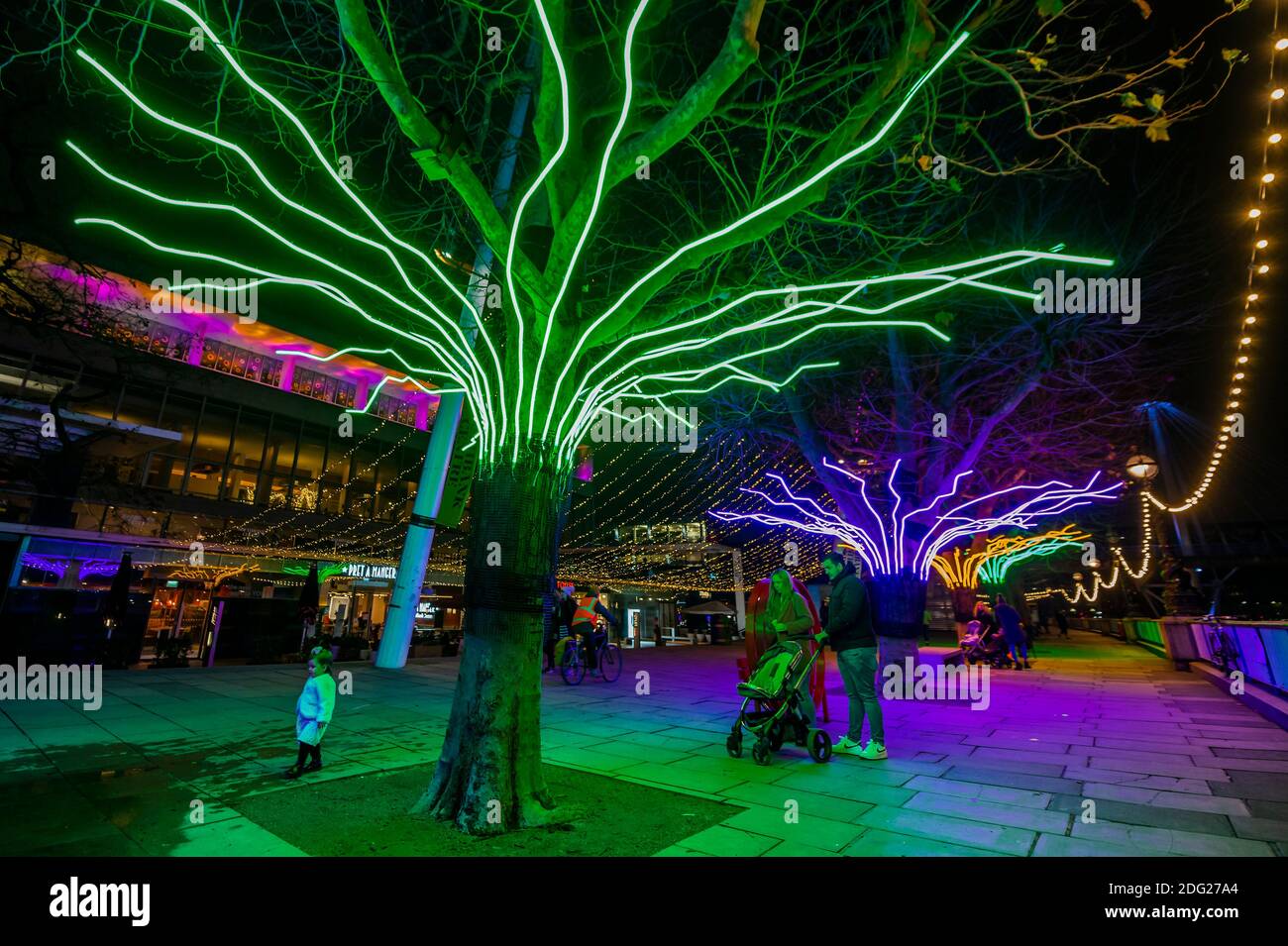 London, UK. 7 Dec 2020. David Ogle's Lumen - A row of the Riverside Plane  trees illuminated with glowing neon flex creating a multicoloured canopy  over the heads of pedestrians with Martin